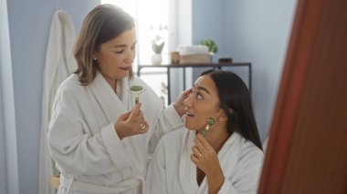 Kadınlar, sağlık merkezinde yüz silindirleriyle rahatlatıcı bir spa gününün tadını çıkarıyorlar. Huzurlu kapalı bir ortamda anne-kız kaynaşma anları sergiliyorlar. Rahat bornozlar ve sakin bir atmosfer.