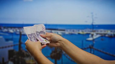 Sahilde çekilmiş İsviçre banknotları tutan bir adamın yakın çekimi, açık hava tropikal ortamında finans ve yatırım kavramını vurguluyor..