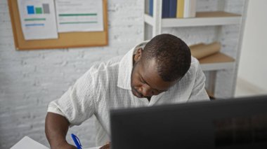 Ofis ortamında profesyonel bir ortamda evrak işlerine odaklanmış notlar yazan genç bir adam yoğun bir çalışma ortamı sergiliyor..
