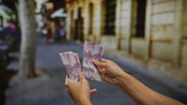 Bir şehir caddesinde Endonezya rupia banknotları tutan adam, şehir dışındaki bir ortamda para birimi detaylarıyla yapılan bir işlemi vurguluyor..