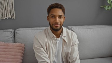 Genç adam modern bir oturma odasında kanepede oturuyor.