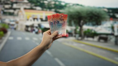 Şehir sokağında elinde İsviçre frangı banknotları tutan bir adam, şehir arka planına sahip açık havada para gösteriyor..