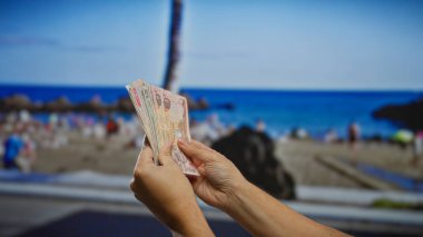 Arka planda bir kumsalda el ele tutuşmak para değişimi anlamında tropikal bir finans ya da iş teması önerir.