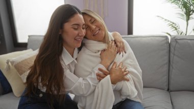 Parlak bir oturma odasındaki rahat bir kanepede sevgi dolu bir şekilde kucaklaşan anne ve kız aile bağlarının sıcaklığını ve yakınlığını yakalıyorlar..