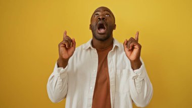 Genç Afrikalı adam heyecanlı bir şekilde izole edilmiş sarı arkaplanı işaret ediyor.