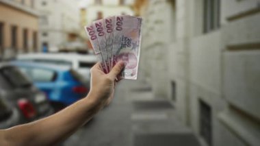 Bir şehir caddesinde Türk lirası banknotları tutan bir adam, şehir dışında araba ve binaların bulanık arka planına sahip bir yerde para gösteriyor..