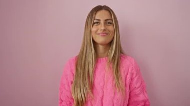 Parmak uçlarında pembe kazak giyen bir kadın izole edilmiş pembe duvar arkasına yaslanmış mutluluk ve pozitifliği gösteriyor. Onaylama ve gençlik enerjisini ifade ediyor..