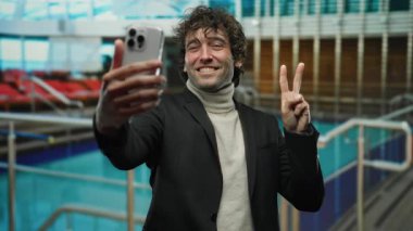 Yolcu gemisinde selfie çeken adam, havuz manzaralı, gülümseyen ve barış işareti yapan açık havada güneşli gökyüzünün altında duran, tatil titreşimlerini ve rahatlığı somutlaştıran..