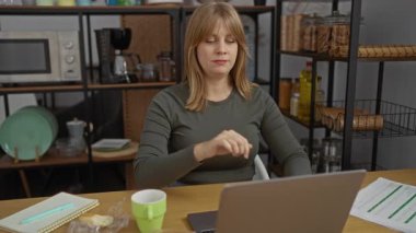 Ofiste dizüstü bilgisayar ve kahveyle rahatlayan bir kadın, huzurlu bir ifadeyle bir an için ara veriyor, mutfak eşyalarıyla çevrili, iş-yaşam dengesini iletiyor.