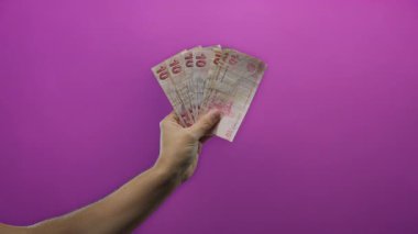 İzole edilmiş mor bir arkaplan karşısında Türk banknotları tutan adam, para birimini net bir şekilde gösteriyor.