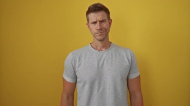 Gri gömlekli genç adam, izole edilmiş sarı arka planda dalgın ve rahat görünüyor. Hafif bir gülümseme, kendine güvenen bir şekilde portre için poz veriyor.