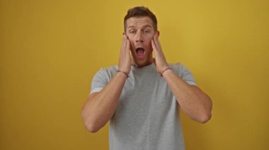 Gri gömlekli genç adam, canlı sarı duvara karşı şaşkınlığını ifade ediyor. Duygularını, şaşkınlığını ve modasını minimalist stüdyo ortamında sergiliyor.