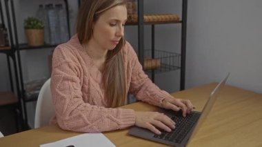 Ofiste çalışan pembe kazaklı bir kadın bilgisayarını ahşap masaya koyup telefonun yanına yerleştirmiş..