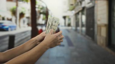 Bir şehir caddesinde Amerikan doları tutan bir adam, açık bir şehir ortamında paralarını sayan elleri gösteren bulanık bir arka plan..
