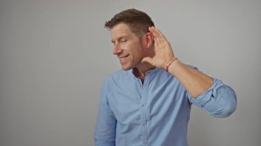 Düz bir duvara karşı gülümseyerek el ele tutuşan açık mavi bir gömlek giyen, izole bir ortamda odaklanmış bir ifadeyle özenli bir jest yapan adam.