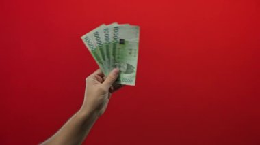Güney Koreli erkek, izole edilmiş bir kırmızı duvara karşı banknotlar kazanarak finansal konsept, para birimi, ekonomi, nakit ve zenginliği basit ve çarpıcı bir şekilde ön plana çıkardı..