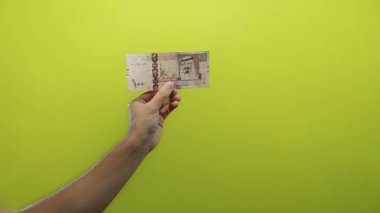 Suudi riyal banknotlarını canlı sarı arka planda tutan adam para birimi detayları ve kültürel öneme vurgu yaparak finansal konsepti yakalıyor..