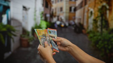 Kentsel bir sokak ortamında Avustralya doları sayan bir adam, açık havada iş ve para alışverişinin özünü yakalıyor ve renkli banknotlarla uğraşıyor..