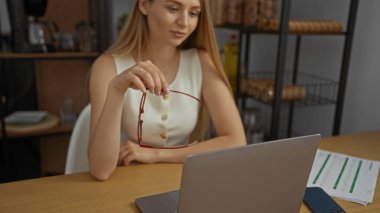 Ofiste çalışan bir kadın, elinde bardaklarla bilgisayar başında modern işyerindeki belgeleri analiz ediyor ve profesyonel çevreye odaklanmayı ve düşünmeyi vurguluyor..