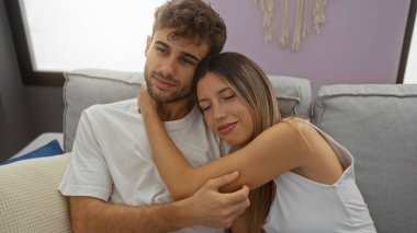 Çift, rahat bir ev ortamında kanepede oturup modern oturma odasında rahatça kucaklaşan erkek ve kadınlara sevgi ve birliktelik gösteriyor..