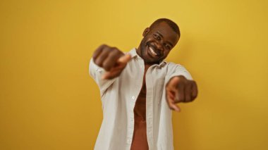 Yakışıklı, Afro-Amerikalı, gülümseyen ve kamerayı işaret eden, sarı renkli bir arka planda izole edilmiş..
