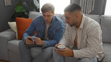 Erkek arkadaşlar oturma odasında oturmuş birlikte akıllı telefonlara bakarken kahvenin tadını çıkarıyorlar.
