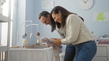 İspanyol çift çocuk odasını hazırlıyor, sevgiyle gülümsüyor ve oyuncakları beşiğe yerleştiriyor, aile sıcaklığını ve şefkatini evlerinde sergiliyor..