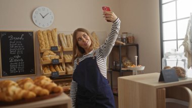 Kadın pastanede selfie çekiyor. Ekmek ve hamur işleri sergileniyor. Menü panosunda fiyatlar yazıyor..