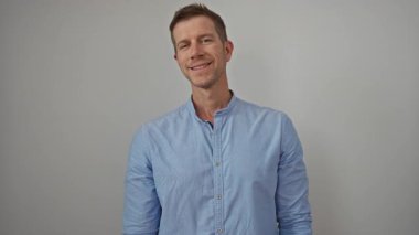 Mavi gömlekli genç adam, arka plandaki düz duvara karşı güvenle gülümsüyor. Modern zarafet ve cazibeyi gösteriyor..