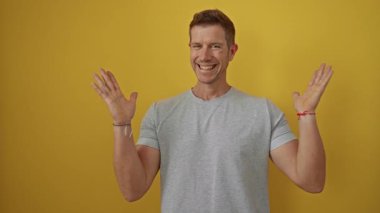 Genç adam neşeli bir şekilde sevinçle kutluyor. Parlak sarı arka plana karşı yumruklarını kaldırarak zafer ve mutluluk anlarını yakalıyor..