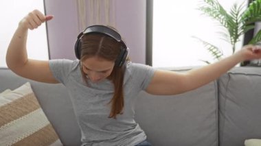 Hoş bir oturma odasında kulaklıkla müzik dinleyen bir kadın dans ederek neşe ifade ediyor. İçerideki rahat koltukta yumuşak yastıklarla çevrili..