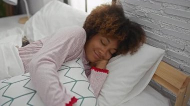 Gülümseyen kıvırcık saçlı, yatakta dinlenen, rahat bir yatak odasında pijama giyen, gündüzleri evde oturan bir kadın..