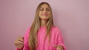 Pembe kazak giyen bir kadın pembe duvarlara karşı alkışlıyor. Gülümsemesi neşe ve pozitifliği yansıtıyor..