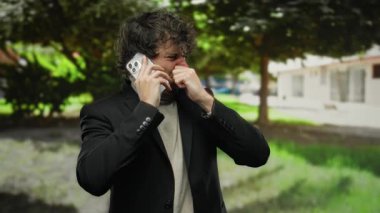 Genç adam açık havada telefonda kötü kokuya tepki verirken burnunu çimdikliyor güneşli bir günde ağaçların altında şehir ortamındaki iğrenmeyi yansıtıyor..
