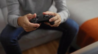 Elinde oyun kumandası olan genç adam, rahat bir oturma odasında oyun oynamaya odaklanmış, konsantrasyon ve rahatlama sergiliyor..