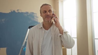 Yeni boyanmış bir salonda telefonla konuşan orta yaşlı bir adam doğal ışıkla rahatlamış ifadesini vurguluyor..