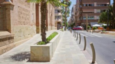 Güneşli bir şehir manzarası var. Palmiye ağaçları, binalar ve kaldırımlar bulanık bir şehir manzarası yaratıyor.