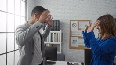 Erkek ve kadın modern bir ofiste sevinçle kutlama yapıyorlar. Kurumsal bir ortamda başarı ve takım çalışmasını ifade ediyorlar..