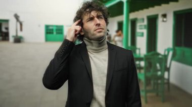 Takım elbiseli genç adam, ev ortamında düşünceli bir ifadeyle fikir jesti yapıyor. İlham ve yaratıcılık duygusunu geliştiriyor..