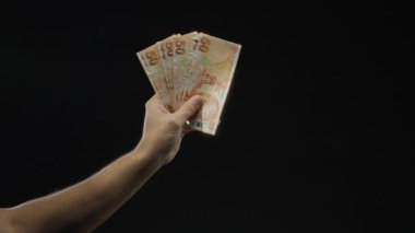 Türk paralarını izole edilmiş siyah arka planda tutan adam, dramatik bir şekilde gölgelenmiş elinde lira banknotları sergiliyor..