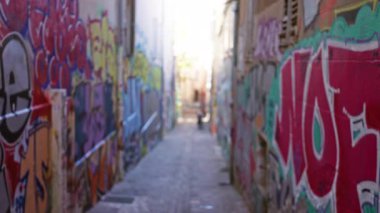 Kentin varoşlarında duvarları renkli graffiti kaplayan ve kaldırım taşı yolda yürüyen insanların odaklanamadığı sanatsal bir atmosfer yaratan bulanık bir cadde..