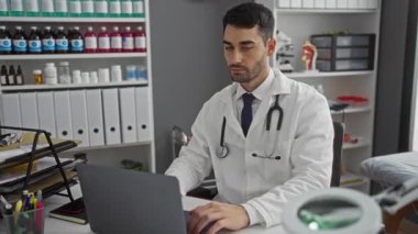 Klinikte çalışan genç yakışıklı bir adam. Masada otururken parmaklarıyla işaret ediyor. Etrafı tıbbî malzemelerle çevrili.