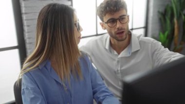 Kadın ve erkek, modern ofis ortamında, bilgisayar başında birlikte çalışıyorlar. Parlak doğal ışık ve profesyonel kıyafetleri var. Kapalı alanda takım çalışması ve işbirliği yapıyorlar..