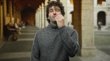 Üniversite ortamında gülümseyen bir adam tarihi bir mimariyle arka planda gri bir kazak giyen, samimi bir an yaşayan insanlar..