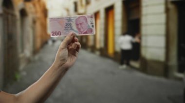Bulanık yayaların şehir ortamında dinamik şehir atmosferi yarattığı hareketli şehir caddesinde el ele tutuşan Türk lirası banknotu..