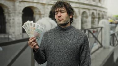 Roma Kolezyumu 'nun dışındaki bir şehir ortamında elinde Czech Koruna banknotları tutan İspanyol bir adam, kültür ve finansmanı yakalıyor..
