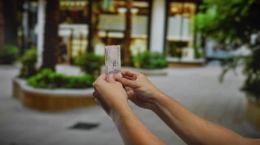 Kentsel bir sokakta Kolombiya pezosu tutan, açık havada banknotları sayan, hareketli bir şehir ortamında finansal işlemleri resmeden bir adam..