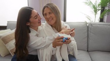 Anne ve kızı sıcak bir oturma odasında kucaklaşıp İspanyol kökenlerini ve aile bağlarını sıcak, huzurlu bir atmosferle sergiliyorlar..