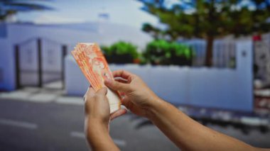 Şehir sokaklarında Filipin pesolarını sayan bir adam, doğal ışık altında renkli banknotlarla kentsel bağlam ve iş alışverişini vurguluyor..