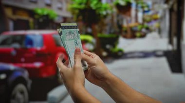 Arka planda bulanık arabalar ve binalar olan bir şehir sokak ortamında Malezya ringgit 'i tutan adam, şehirde bir iş alışverişini vurguluyor..